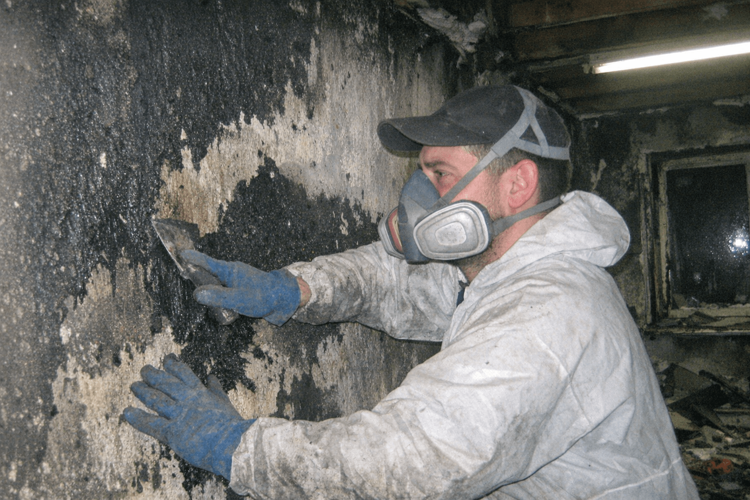 Dunkle Rußspuren an Wänden, während ein Mitarbeiter verbrannte Gegenstände aus einem Zimmer trägt.